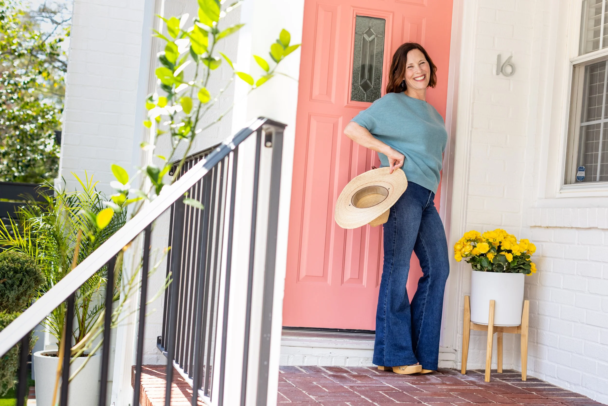 Ann, founder of The Southern Zen, standing on the front porch of the Charleston venue in front of a bright red door surrounded by greenery.