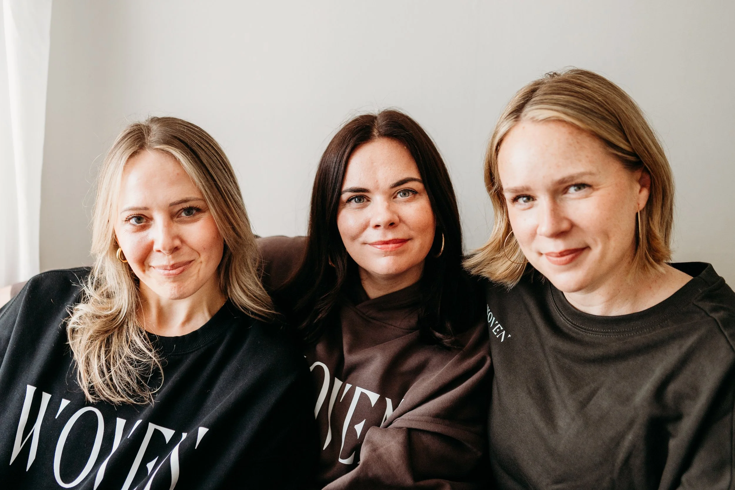Three women sitting close together on a couch, smiling at the camera.