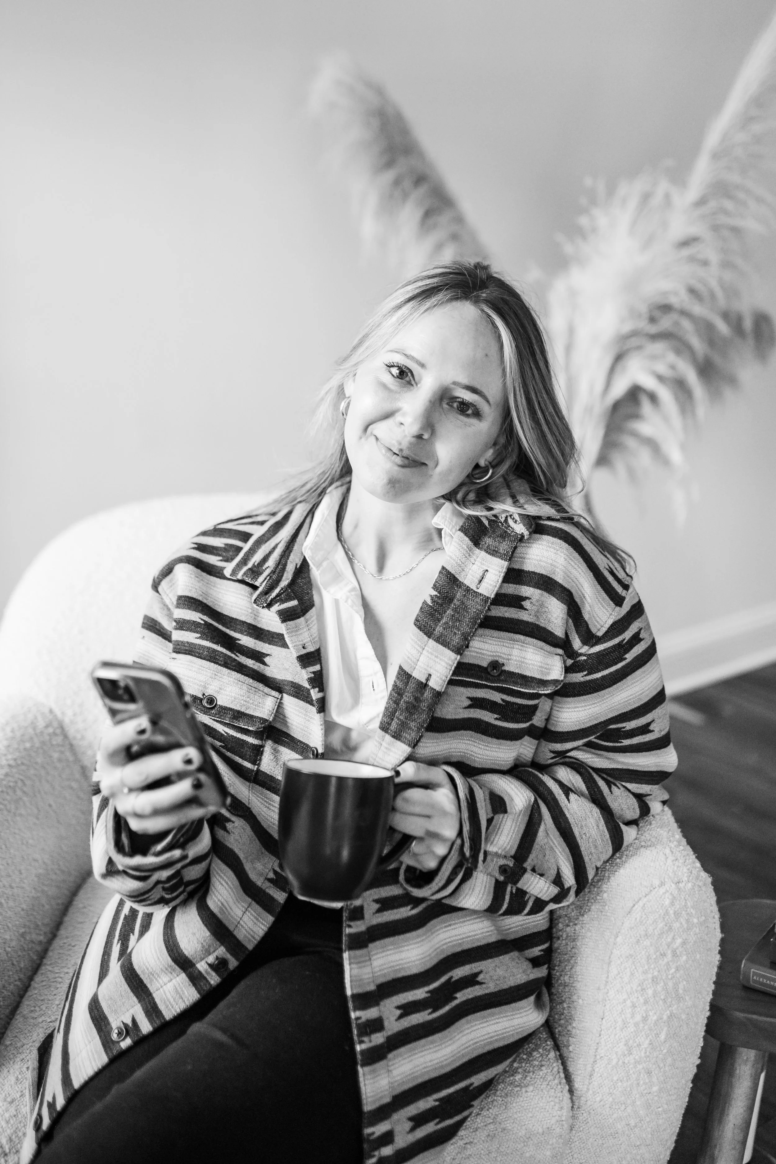 Black and white photo of woman with a phone and coffee cup