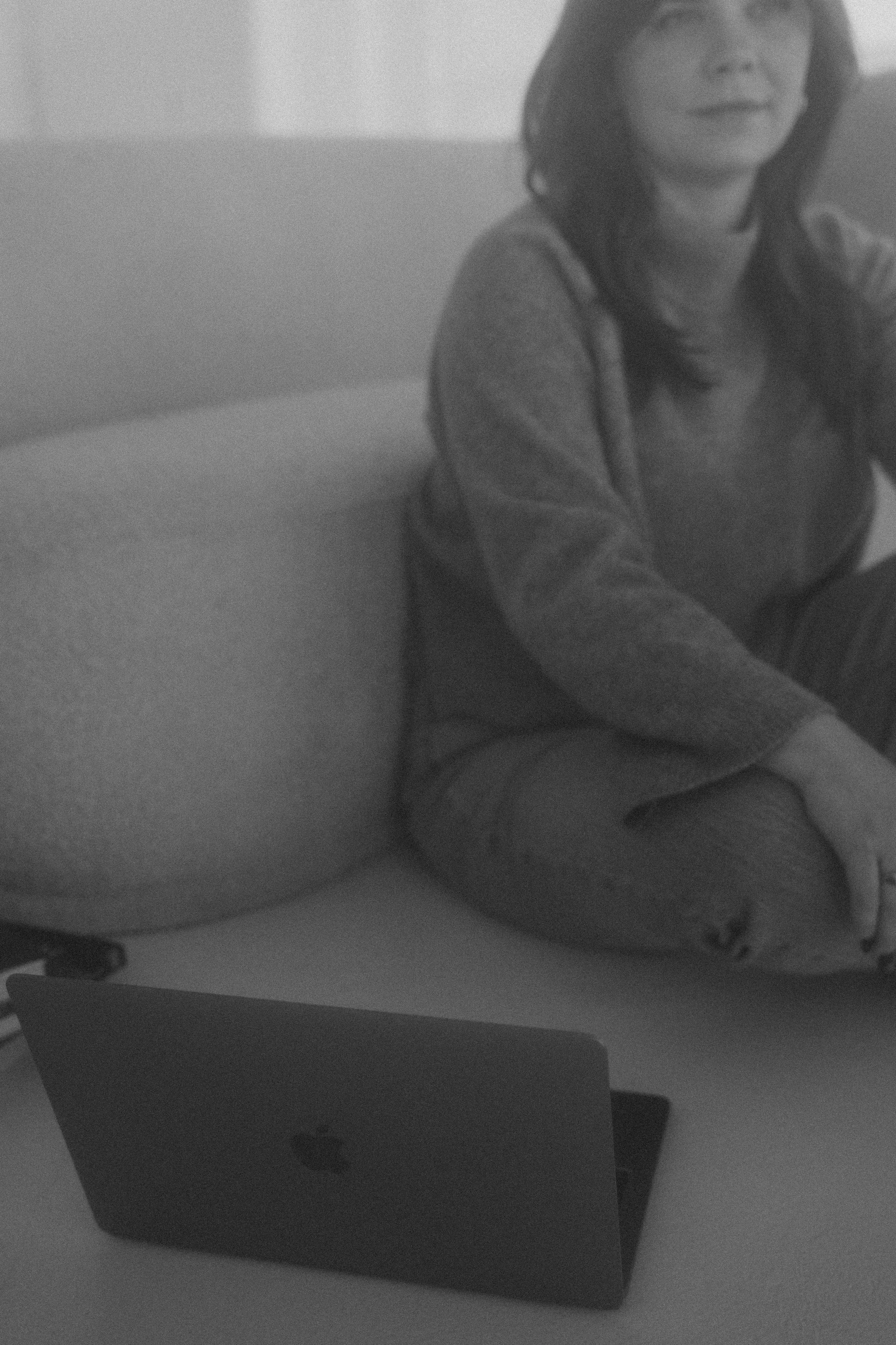 A woman sitting on a couch with a laptop on a table in front of her, in a casual indoor setting.
