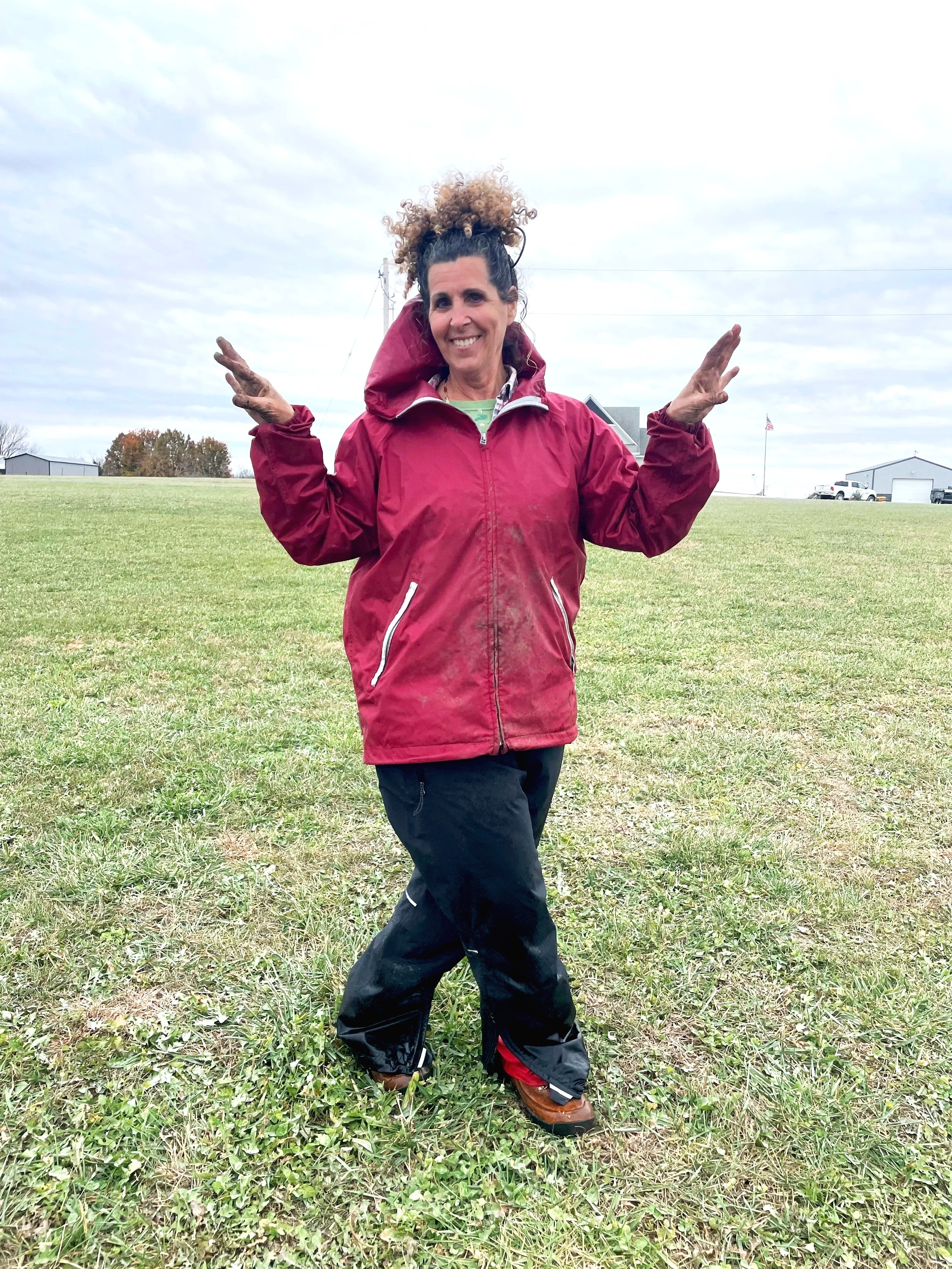 A woman with curly hair smiling and holding two pink embroidered towels that read 'The Queen Has Retired' and 'If You Can Read This' in a cozy kitchen.