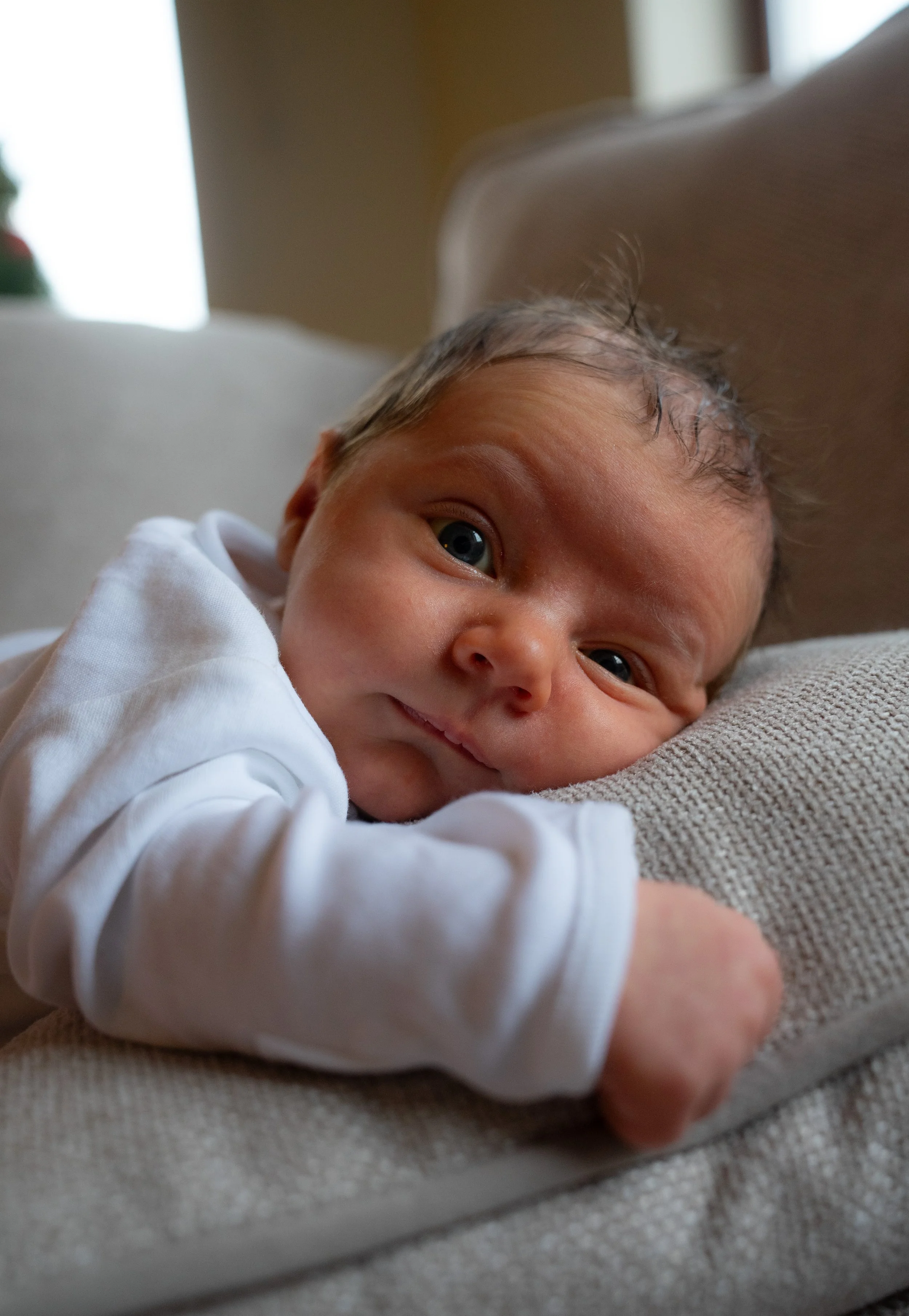 Close-up of a newborn baby lying on a couch, gazing at the camera with a curious expression.