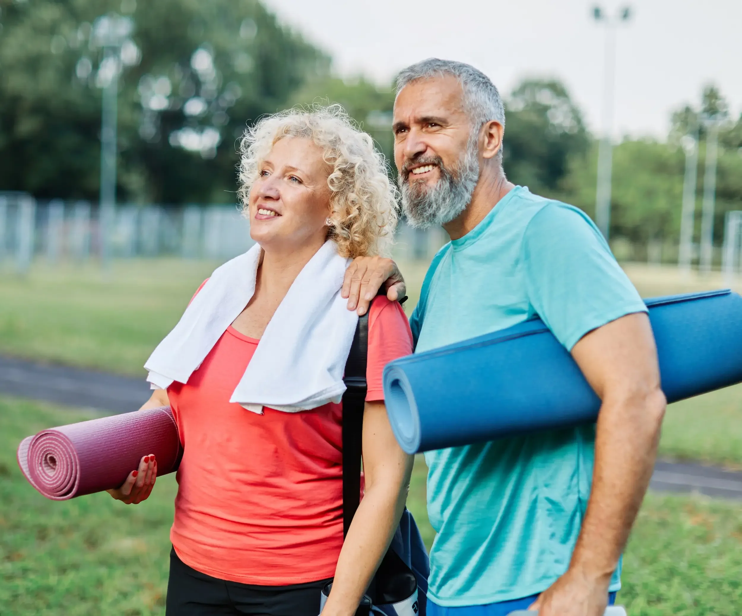 Active middle aged couple with yoga mats in the park.