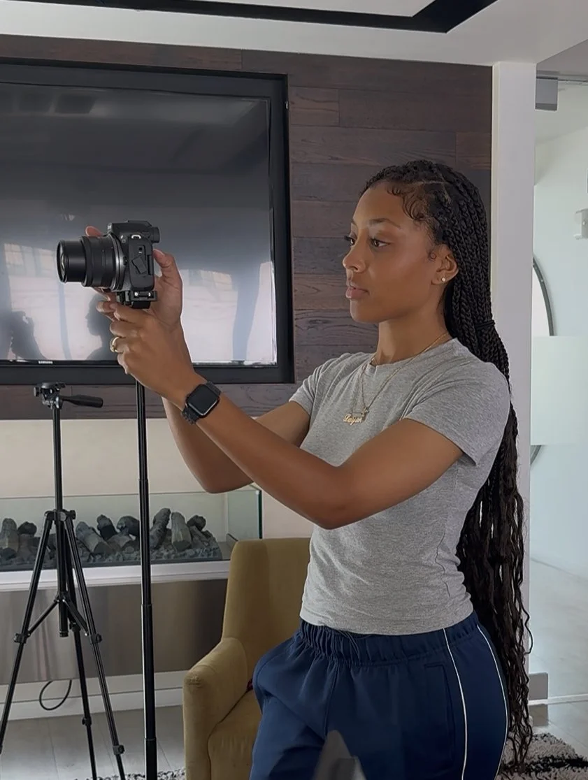 A woman with long braided hair taking a photo with a camera in an indoor setting.