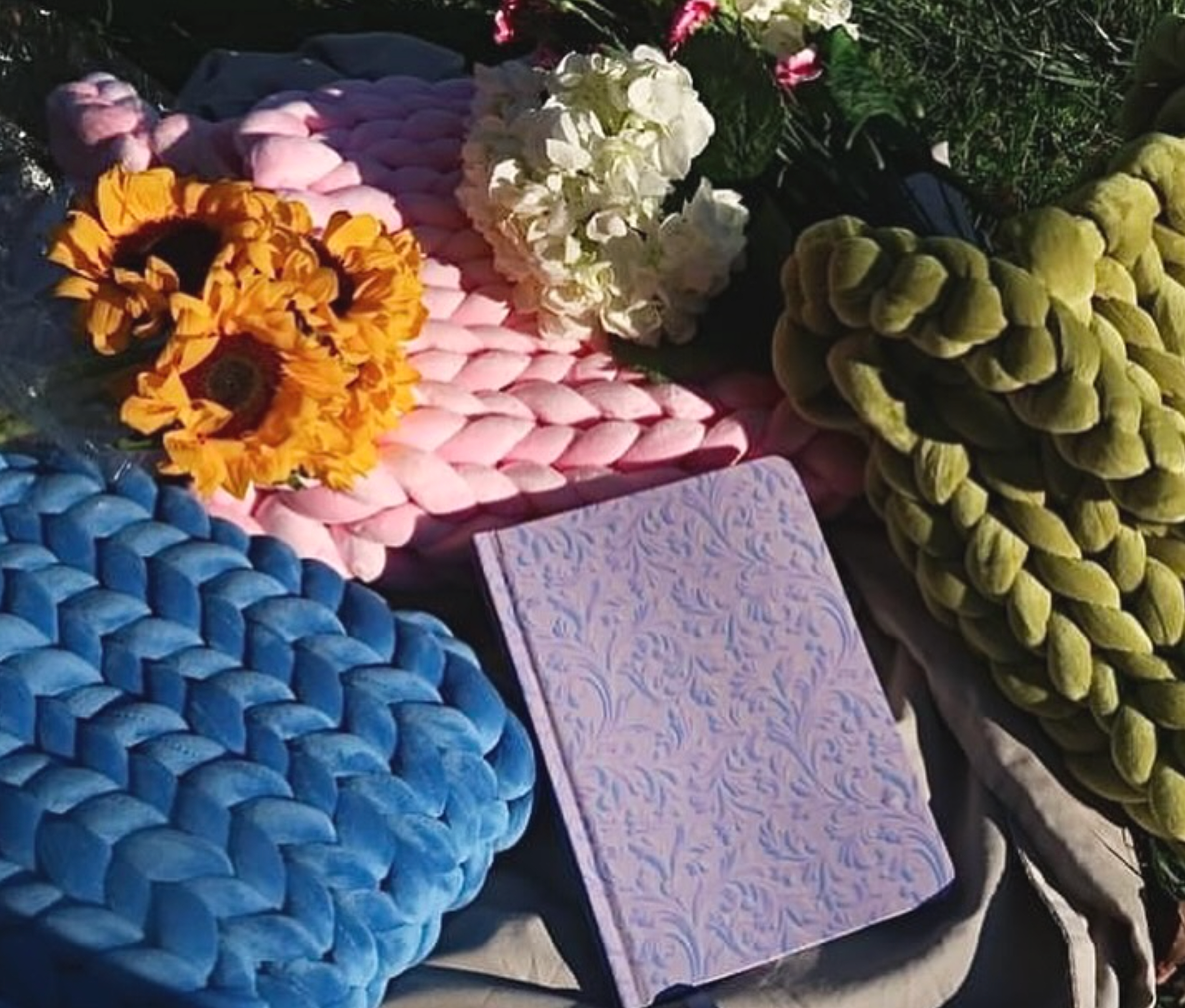 Colorful woven handbags with floral arrangements on top, including sunflowers and white hydrangeas, displayed on a table.