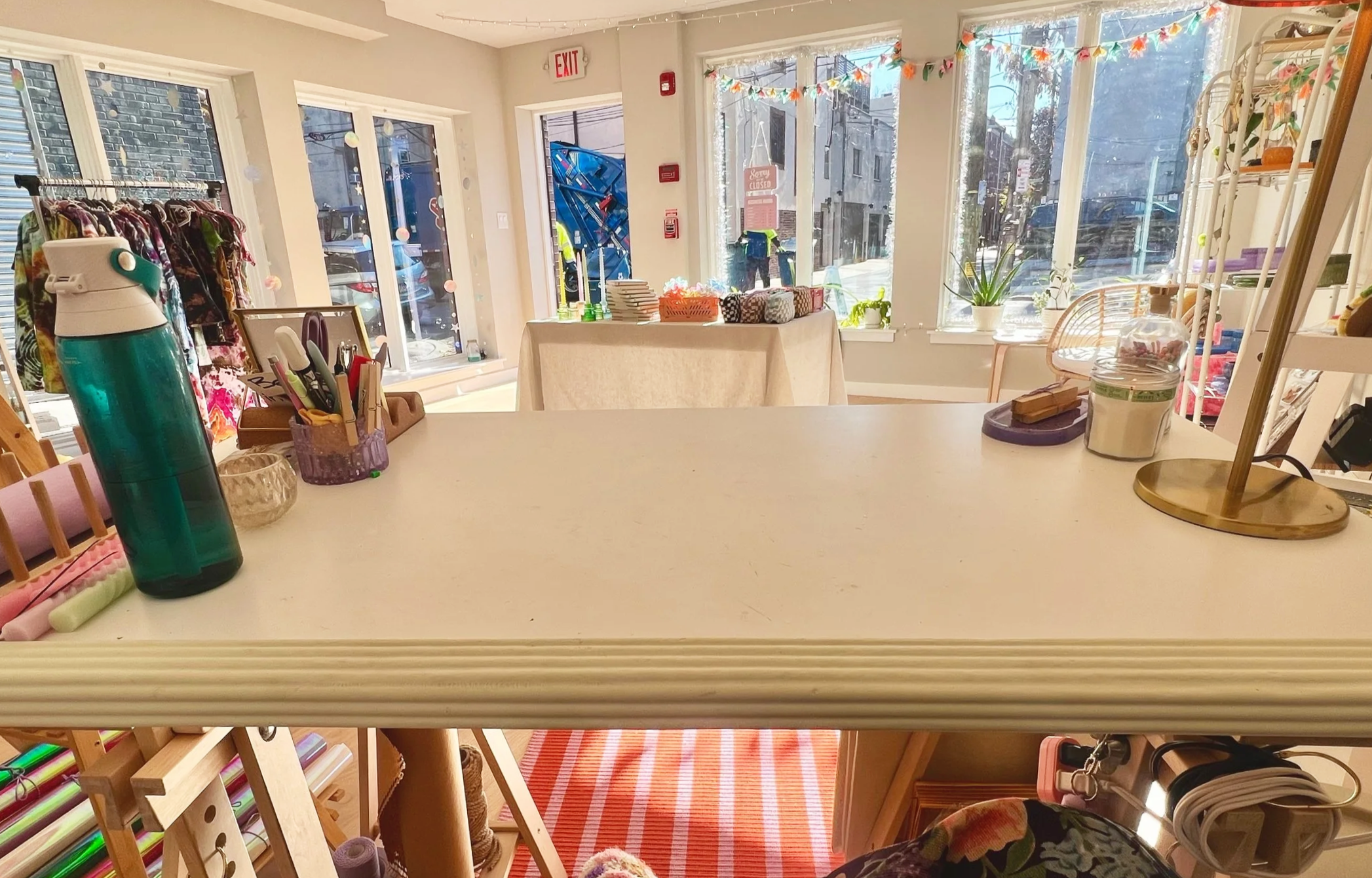 Interior of a colorful boutique or craft shop with large windows, display shelves, and a table with wrapped gifts and decorative items.