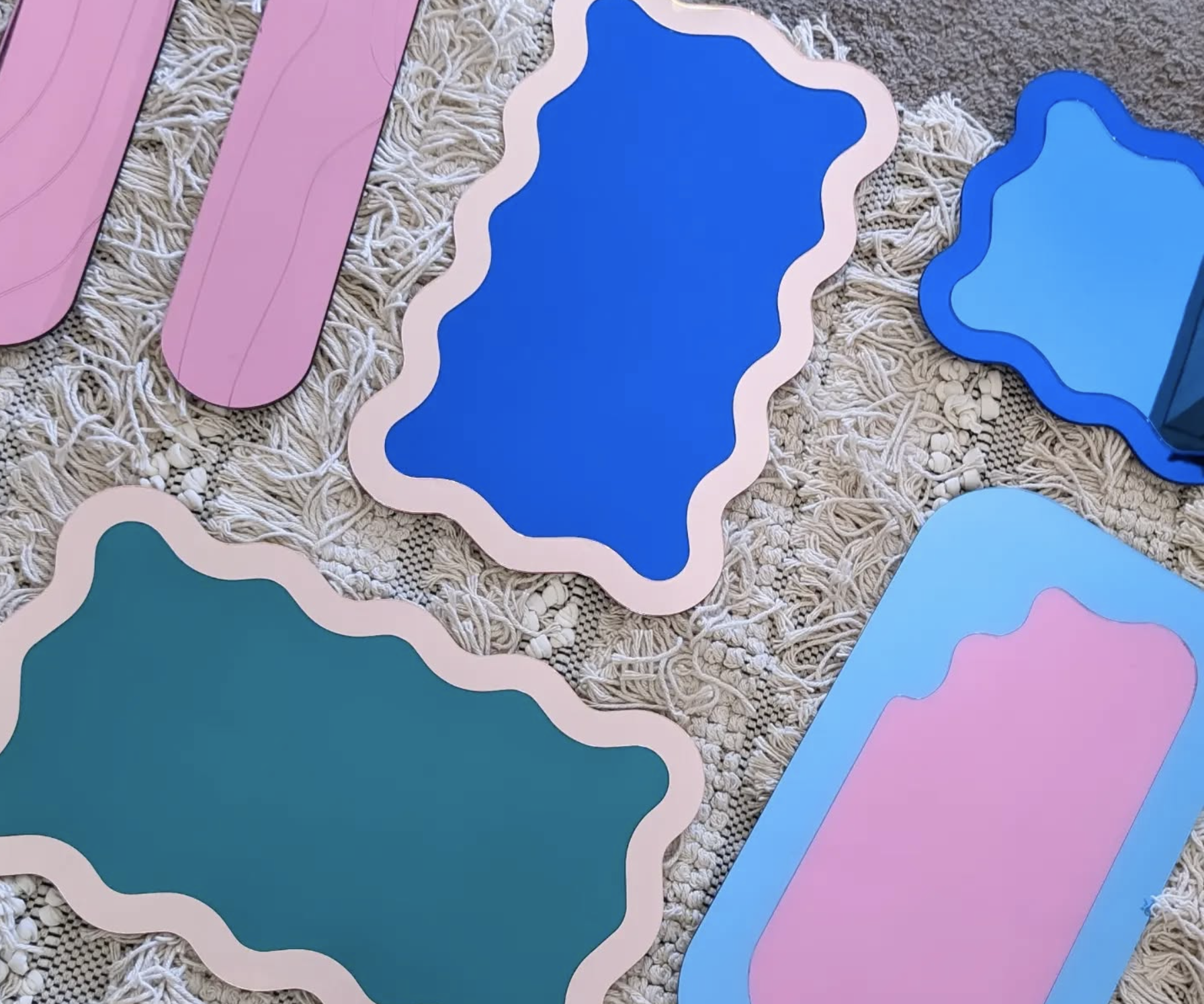 Colorful mirrors with wavy and oval shapes arranged on a textured surface.