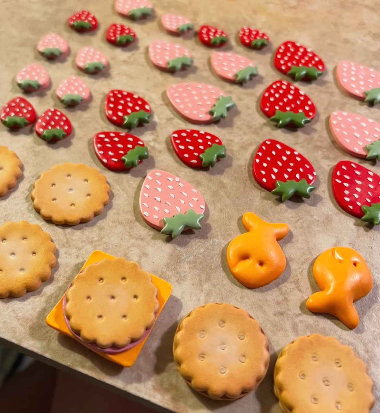 Assorted strawberry-shaped and round cookies and candies arranged on a baking sheet, with some cookies stacked in an orange container.