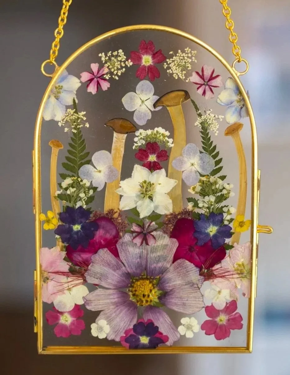 Pressed colorful flowers displayed in a glass and gold frame case.