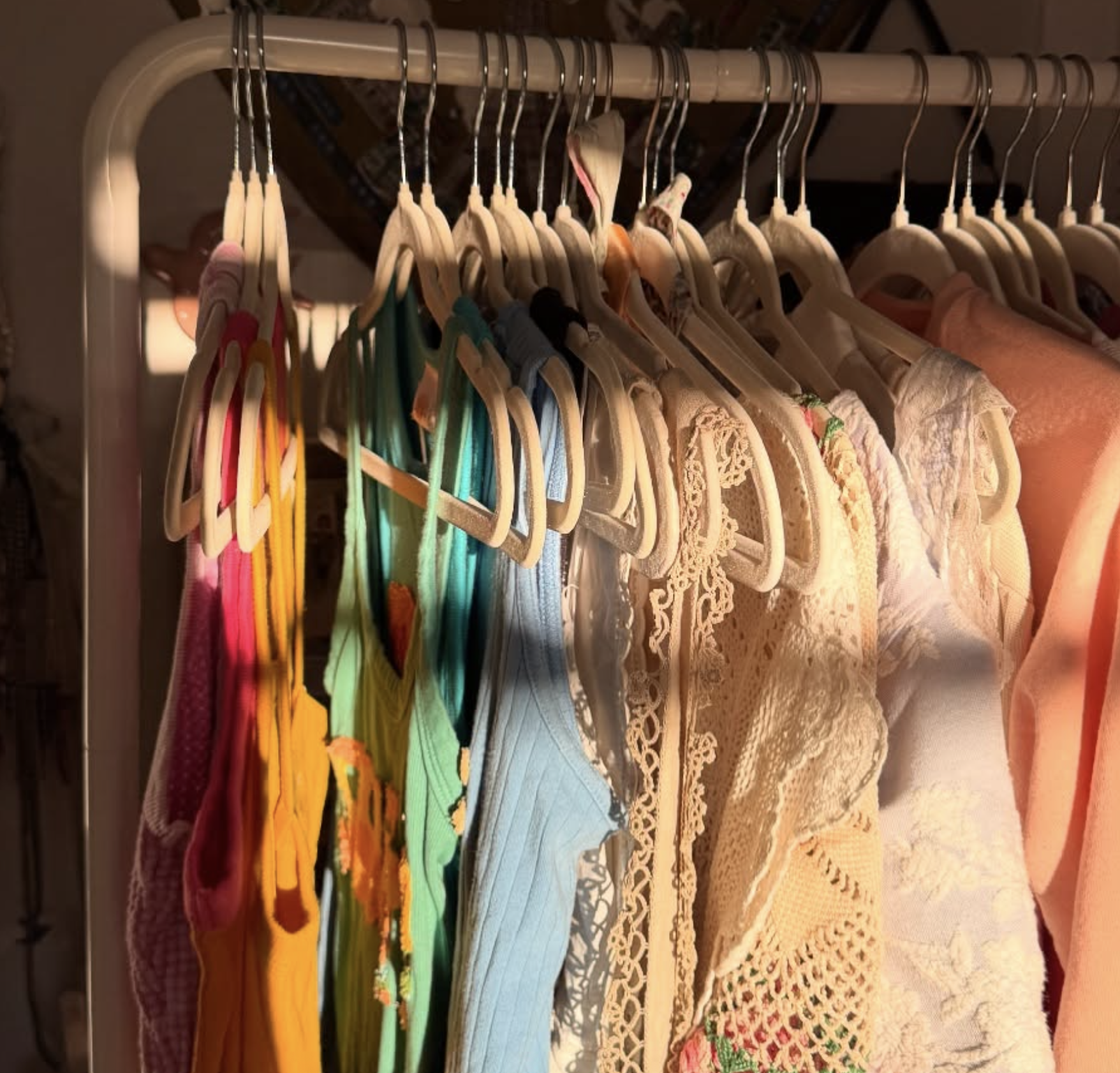 Clothing rack with colorful dresses and tops on wooden hangers, illuminated by warm light.