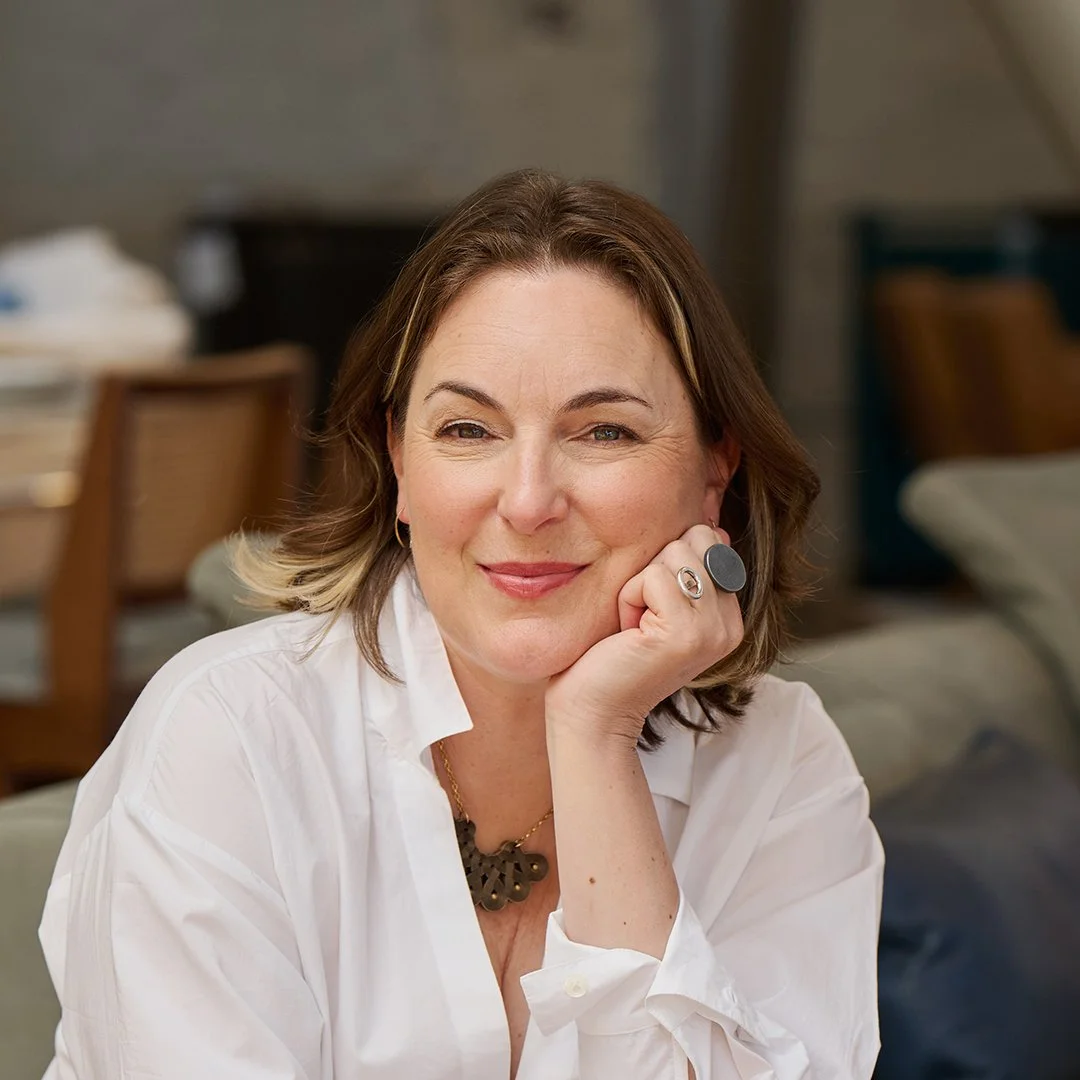 Professional headshot of a woman wearing a black blouse with a patterned collar, set against a softly blurred neutral background.