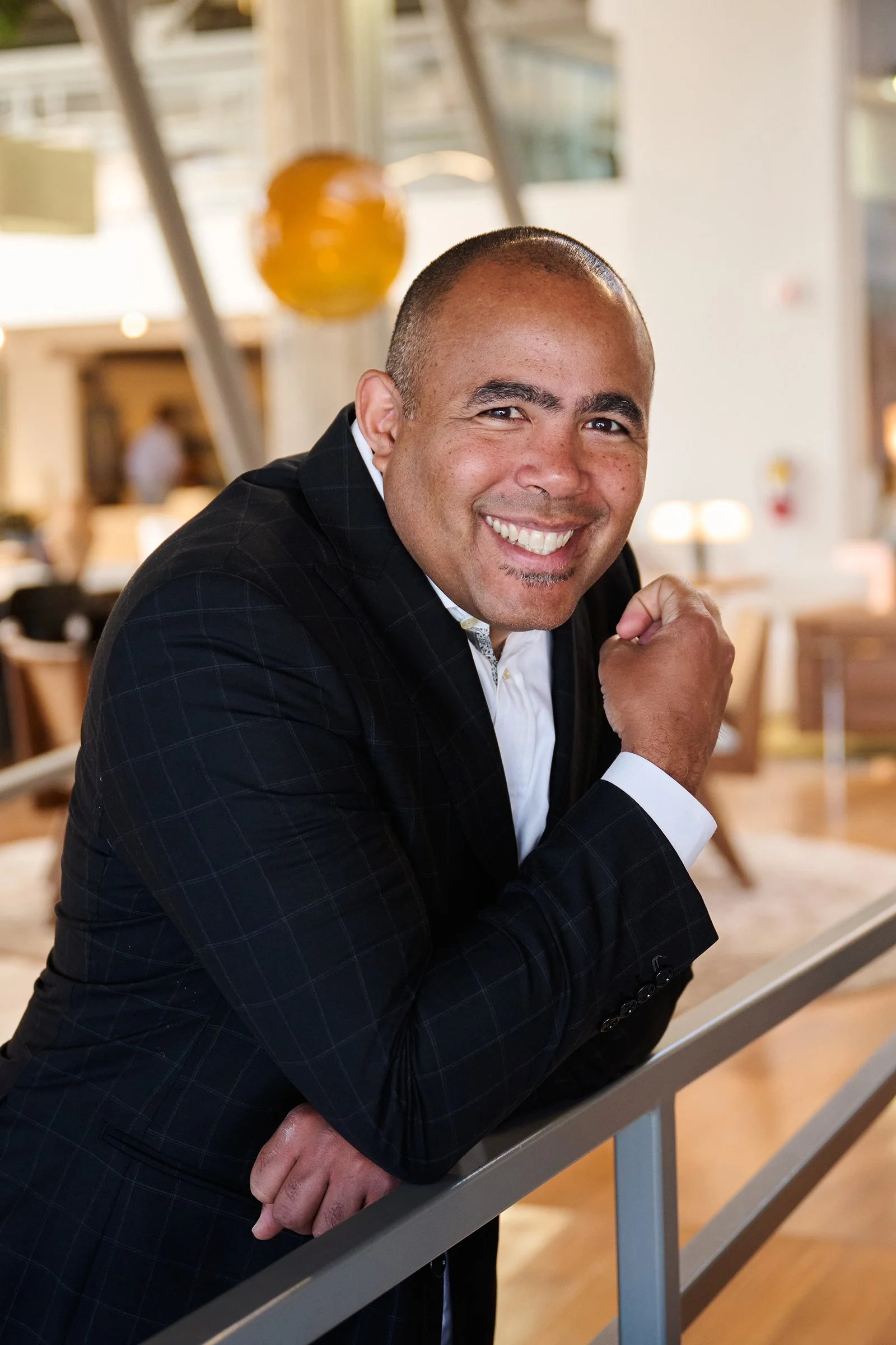 Smiling man in a dark suit leaning on a railing in a bright, modern interior