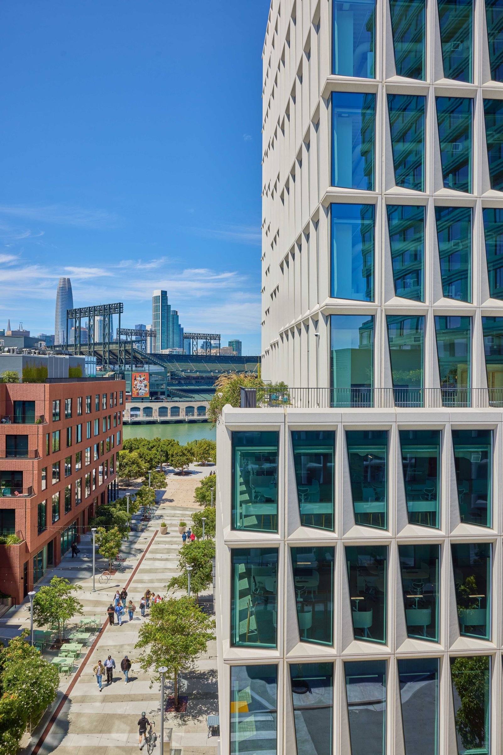 Mission Rock Block G facade overlooking a pedestrian promenade, Oracle Park, and the San Francisco skyline.