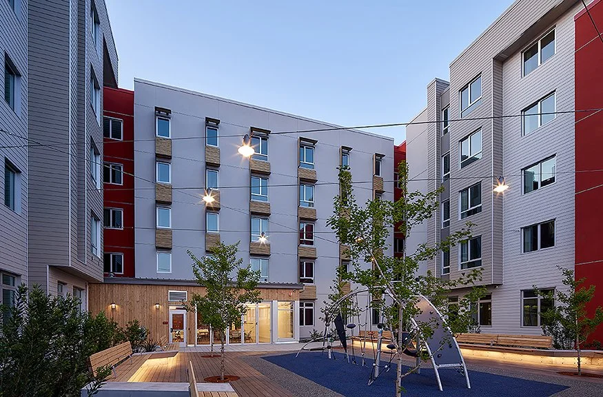 Landscaped residential courtyard with play equipment, benches, young trees, and surrounding multifamily housing.