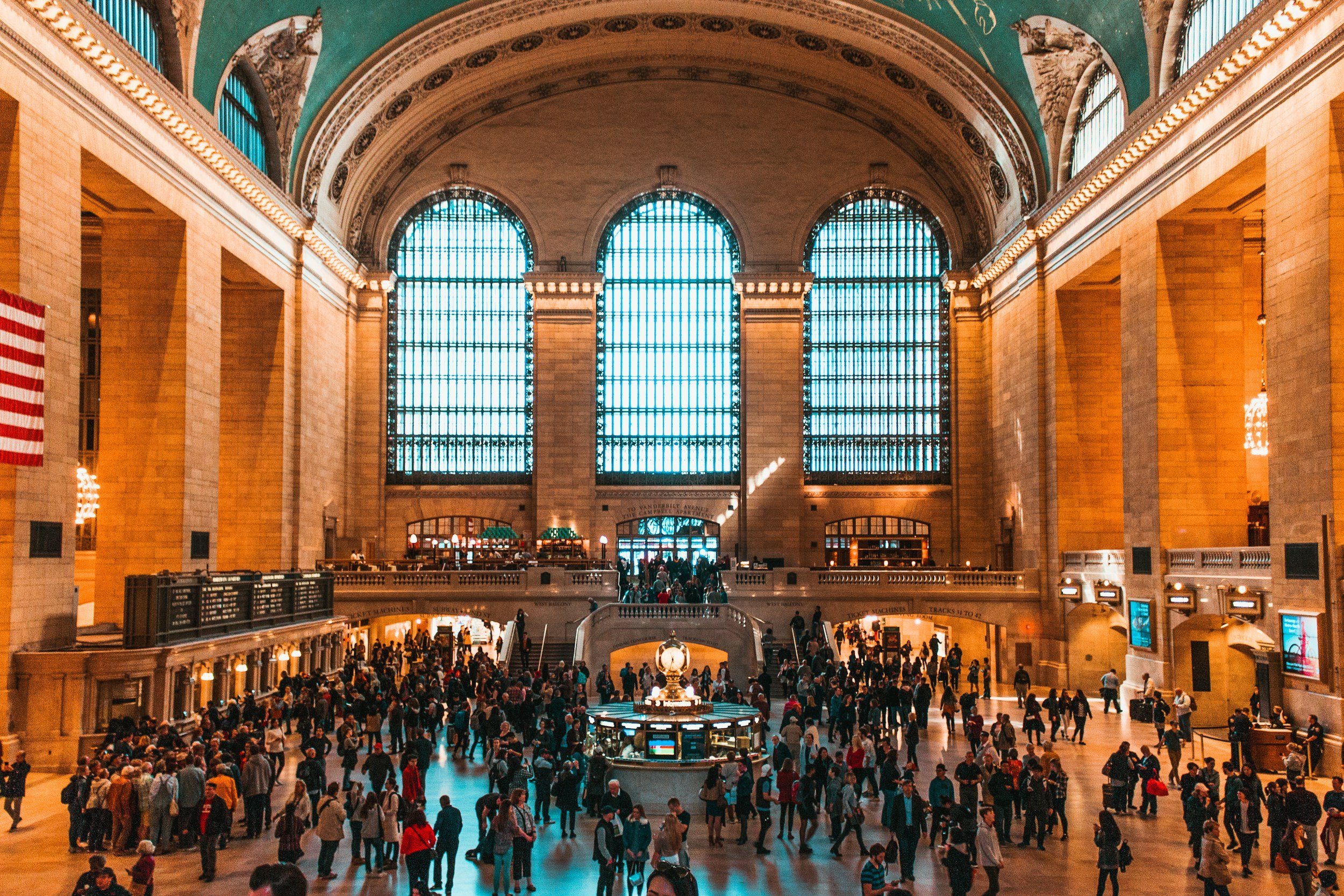Grand central station interior with high arched stained glass windows and a crowd of people inside.