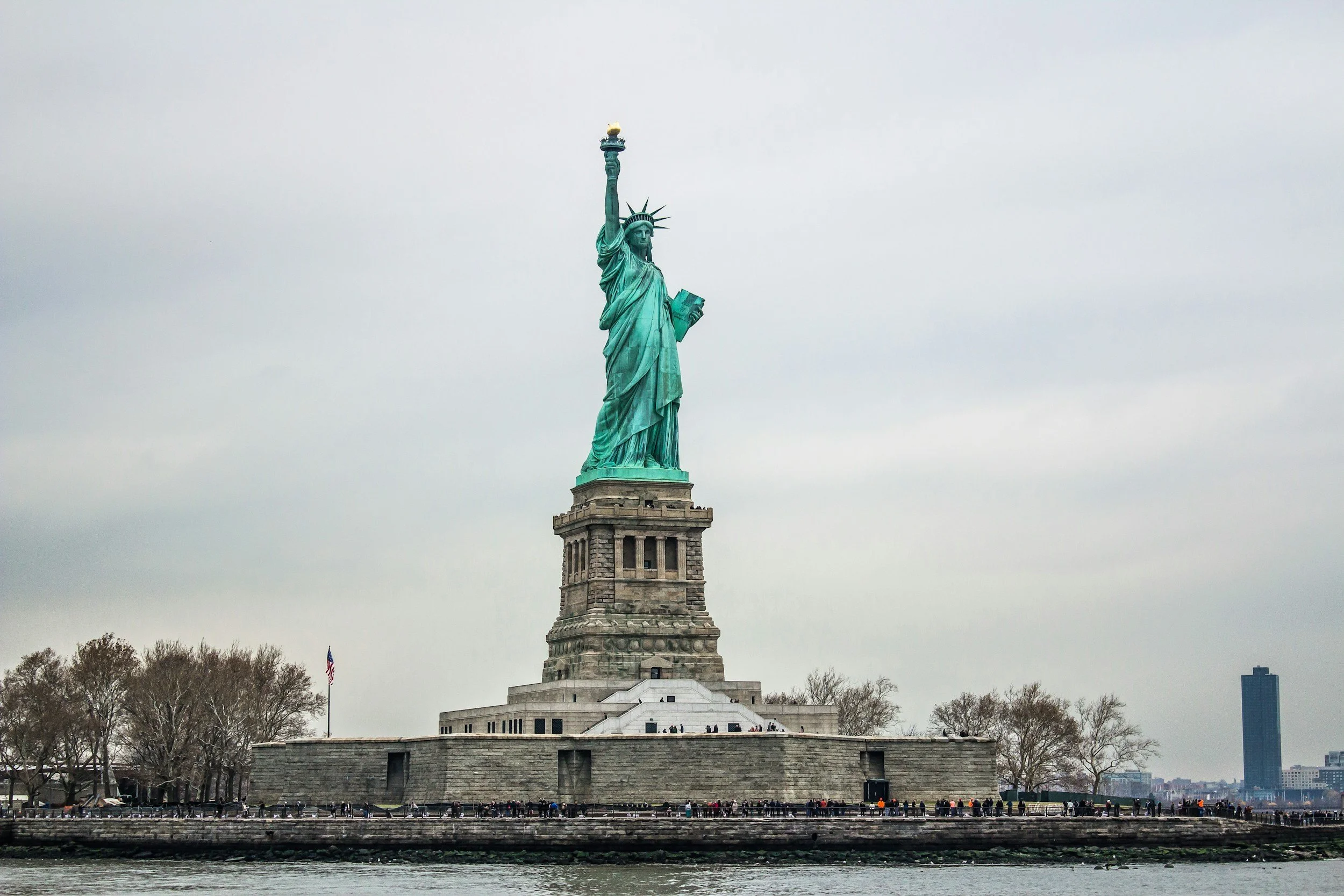 The Statue of Liberty standing on Liberty Island with a cloudy sky overhead.