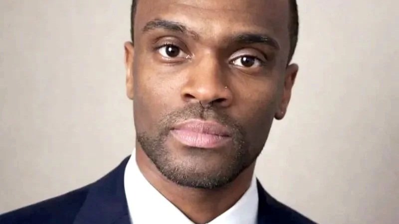 A man in a suit and tie looking directly at the camera with a neutral expression.
