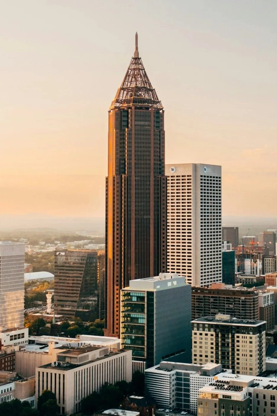 Skyline of a city with a tall skyscraper during sunset, surrounded by other high-rise buildings.