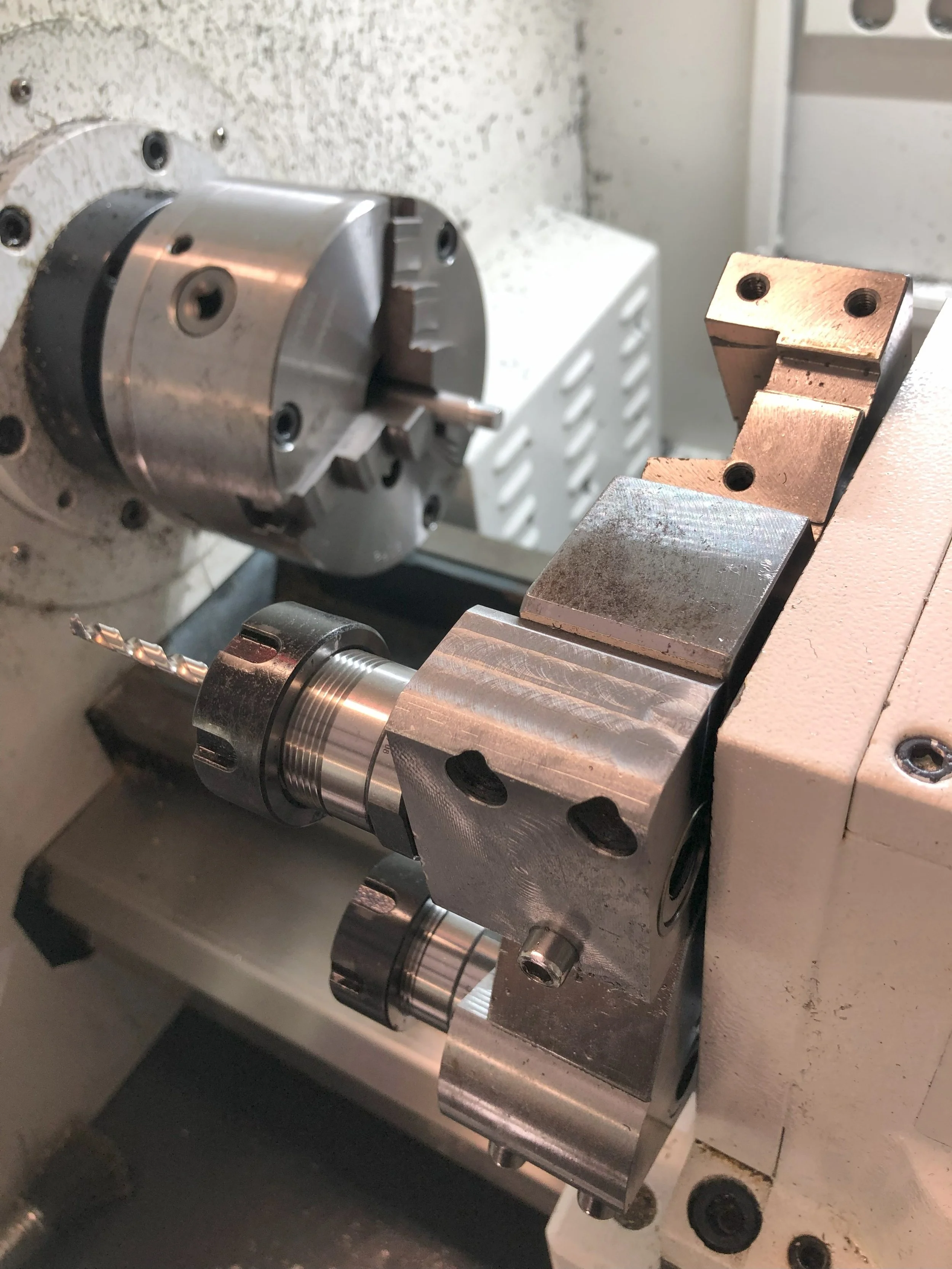 Close-up of a metal lathe machine with a drill bit and chuck mounted on it.