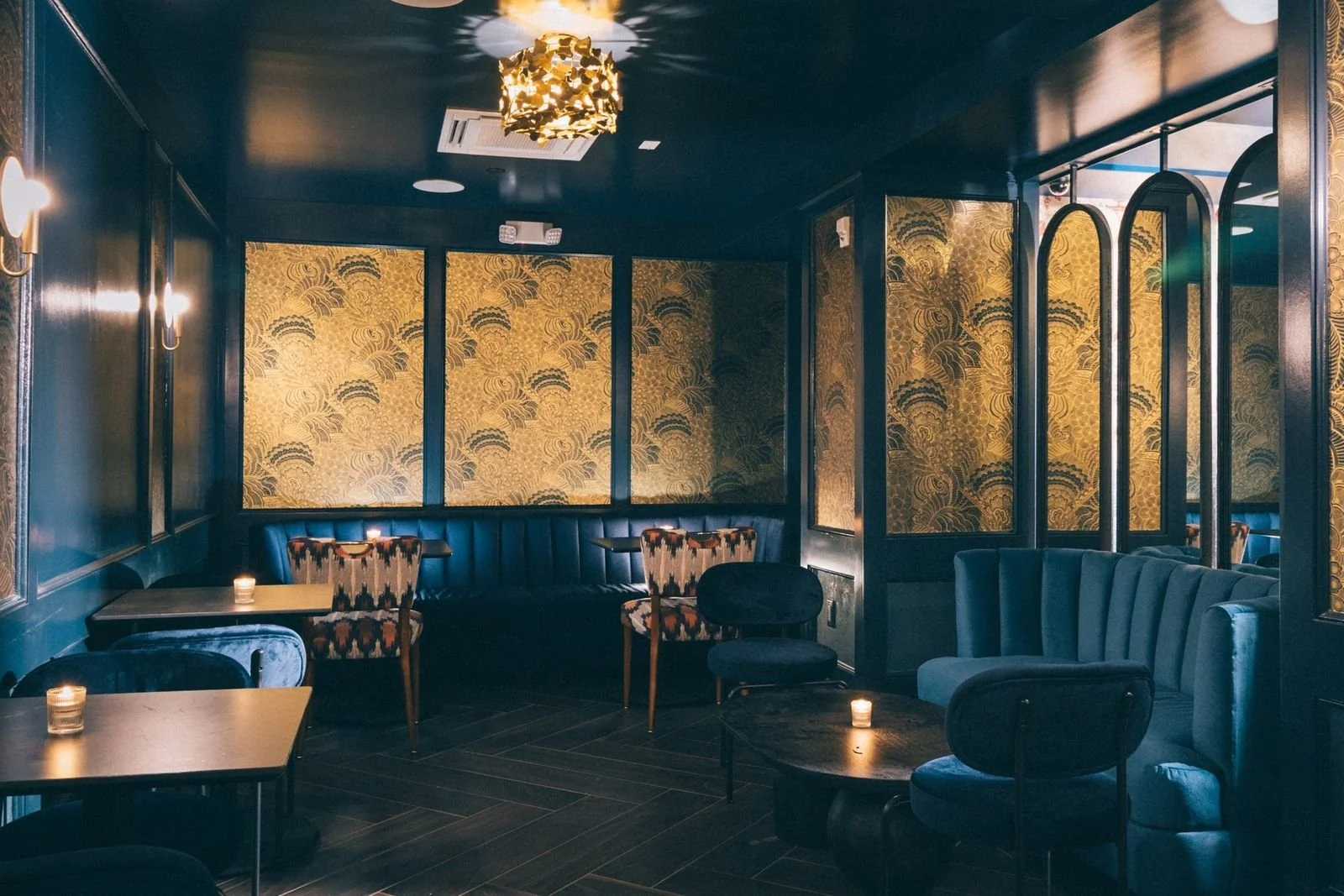 Teal velvet chairs under a gold chandelier and patterned gold wallpaper