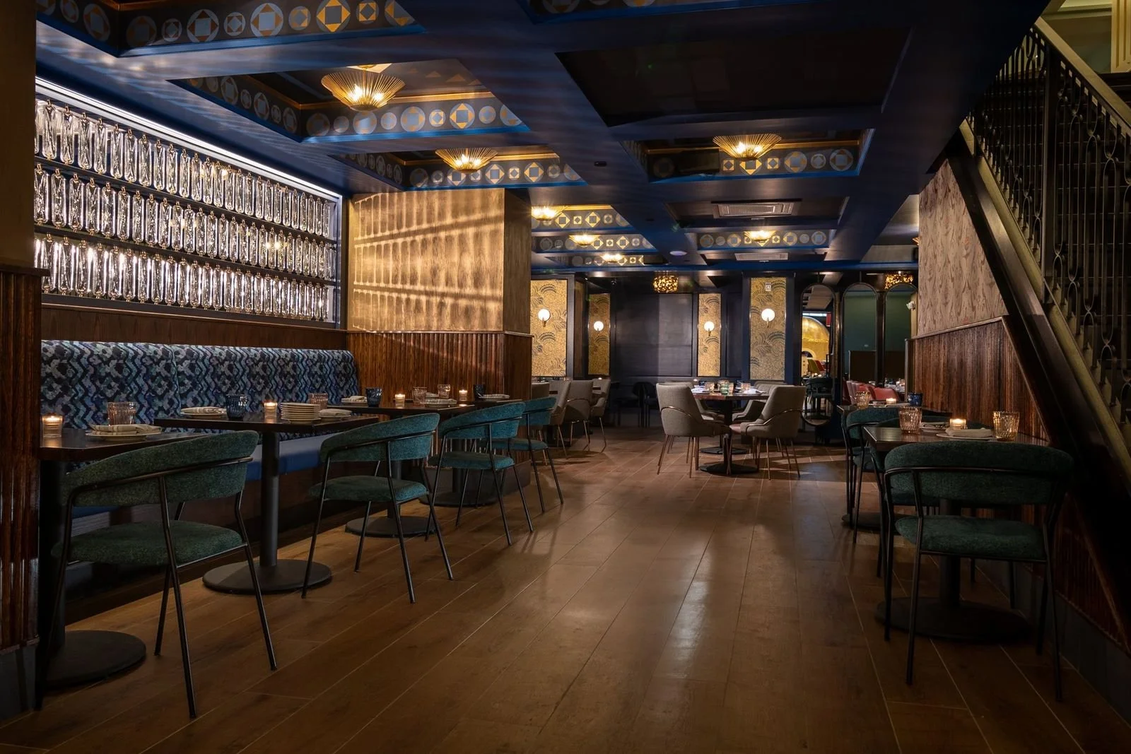 A long teal room with a lit bottle wall and brass pendants