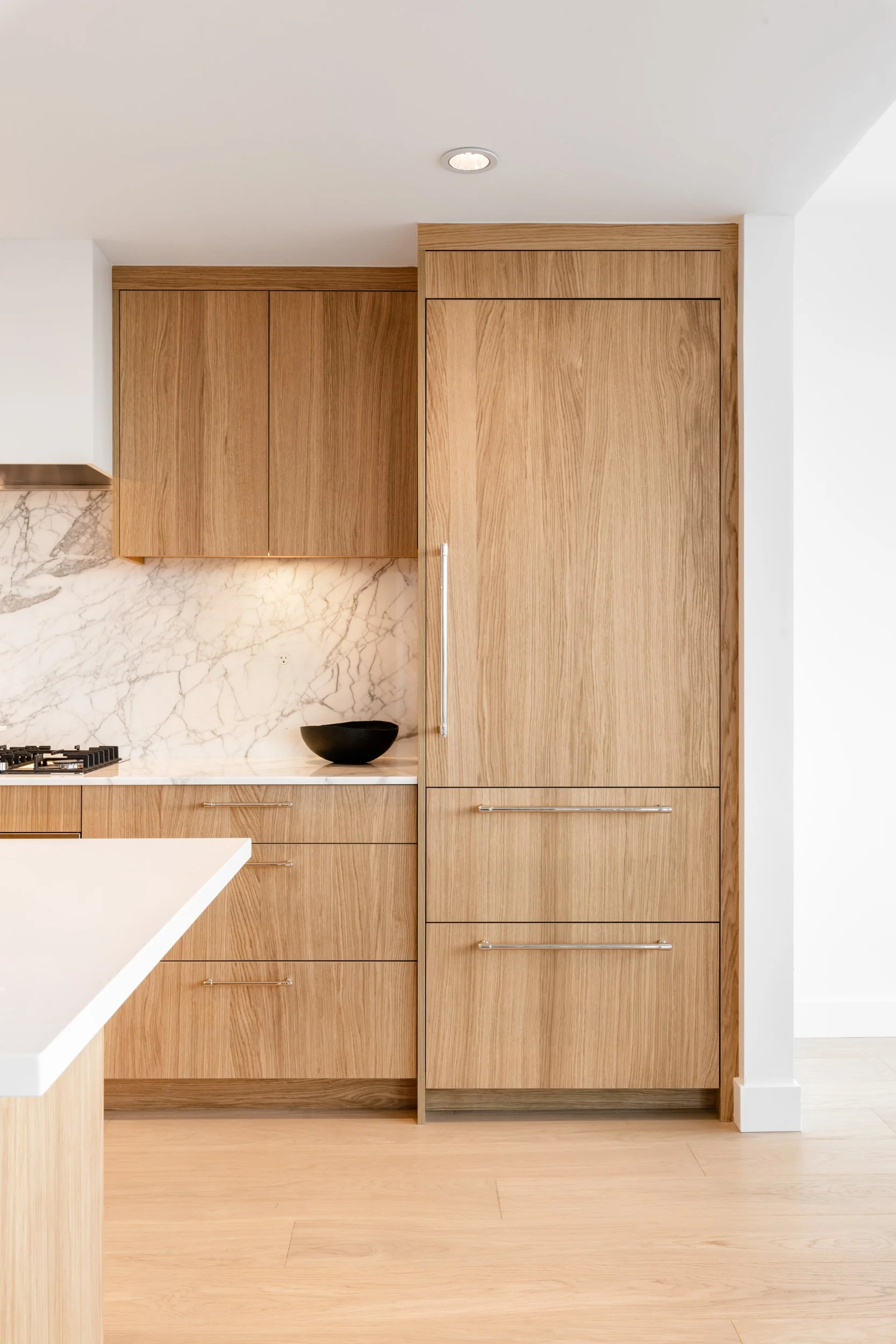 Kitchen with light wood cabinets, marble backsplash, and a black bowl.