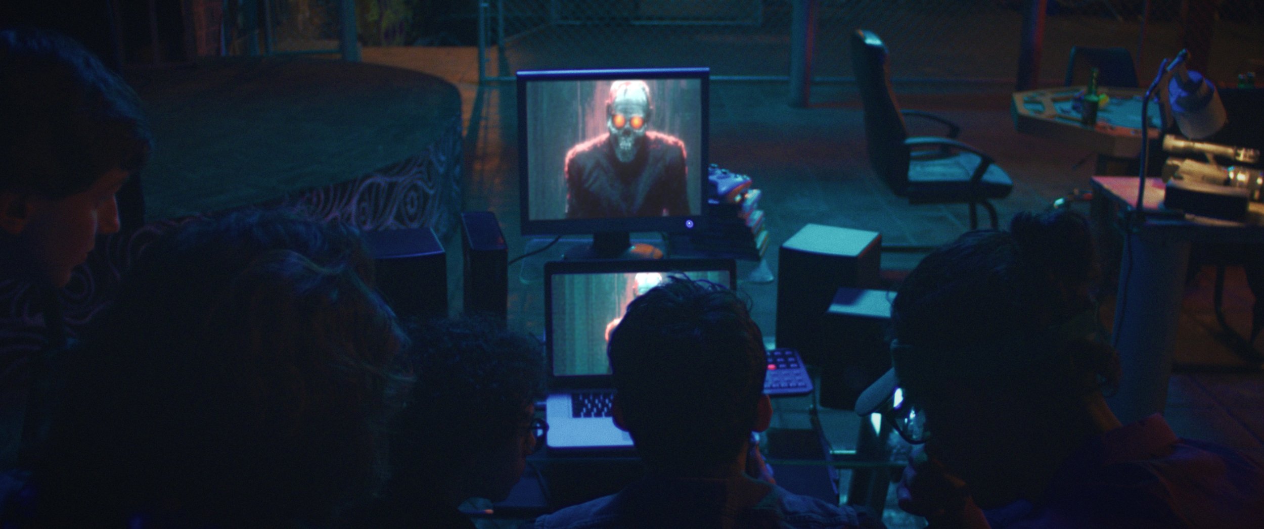 The Nation - Un grupo de personas viendo una pantalla de televisión que muestra una figura de un robot con ojos brillantes en una habitación con iluminación tenue, en un entorno que parece ser una sala o sala de juegos.