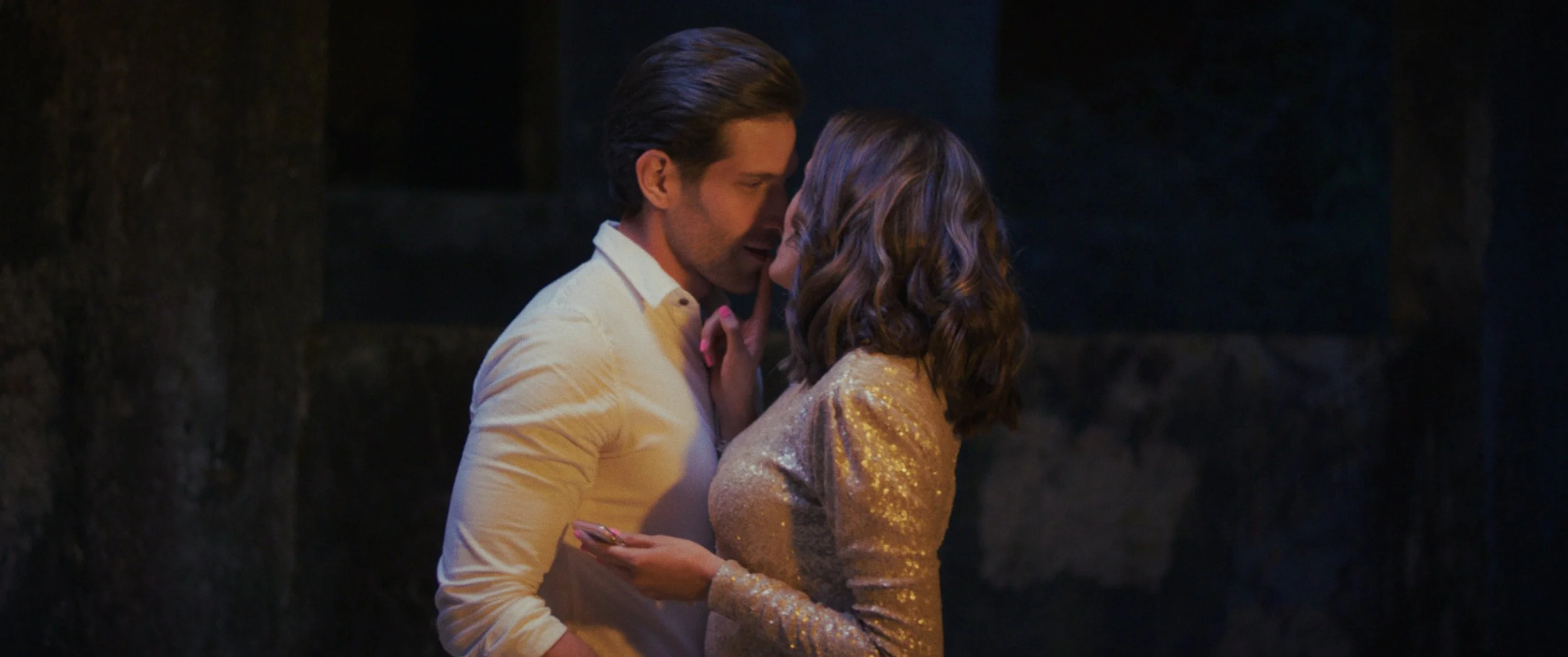 The Nation - Bárbara Islas y Manuel Riguezza - Una pareja, un hombre y una mujer, se abrazan y se miran con cariño en un ambiente romántico y oscuro, probablemente en la noche o en un lugar con poca iluminación.