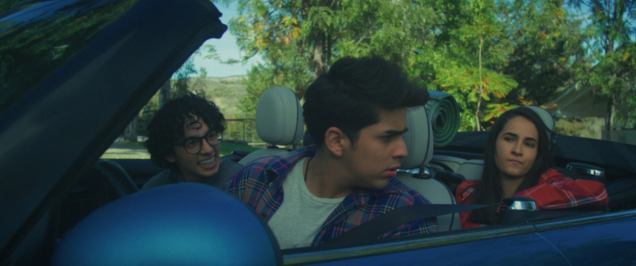 The Nation - Tres jóvenes sentados en un coche, uno de ellos en el asiento del conductor, en un día soleado con árboles verdes en el fondo.