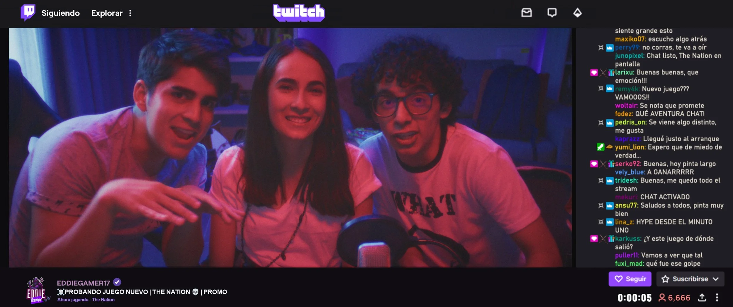 The Nation - Tres personas sonriendo y mirando hacia la cámara en una transmisión en vivo en Twitch, con un chat en el lado derecho y fondo oscuro con iluminación colorida.
