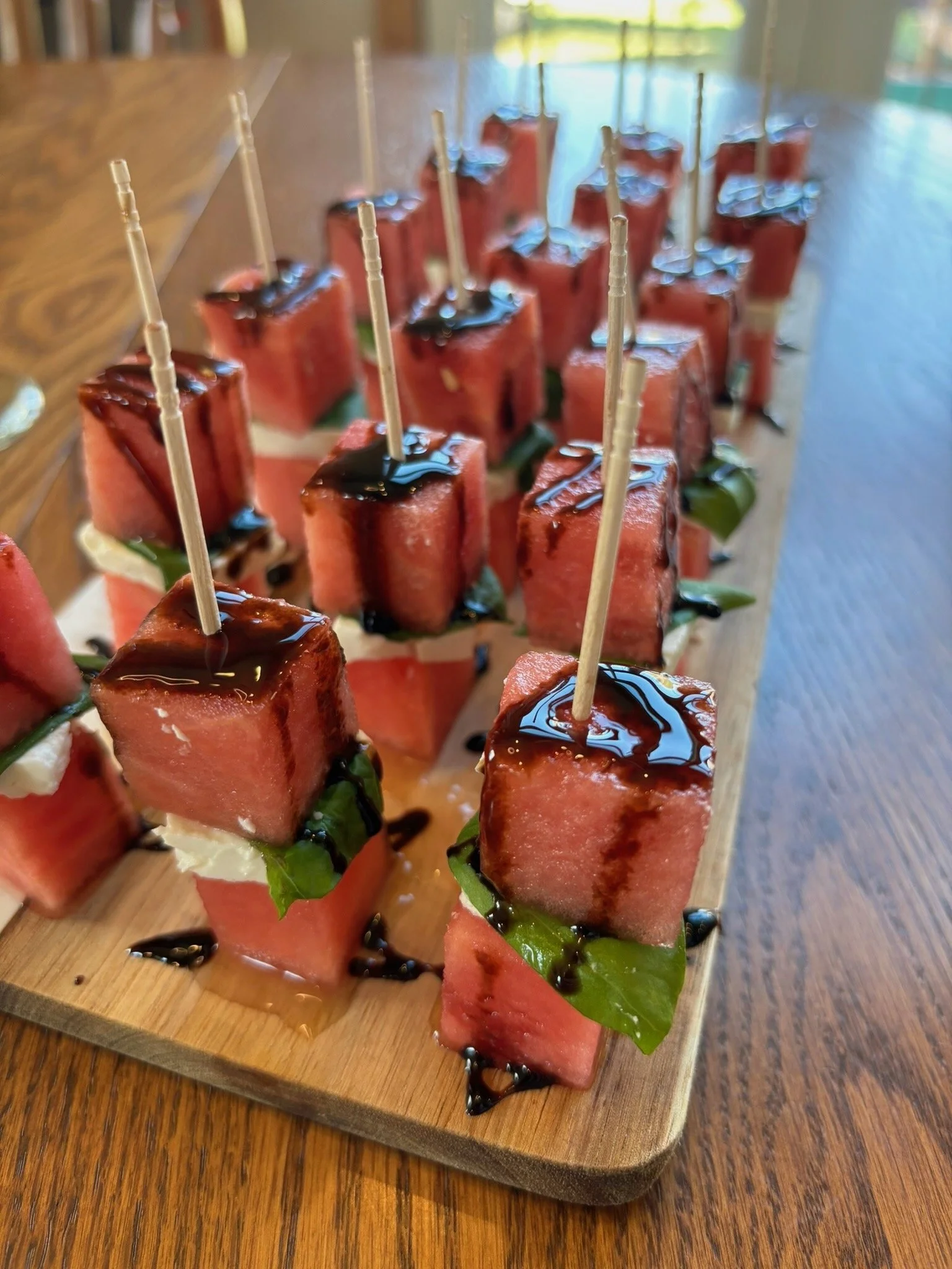 Watermelon and feta appetizers on skewers with basil and balsamic glaze on a wooden board.