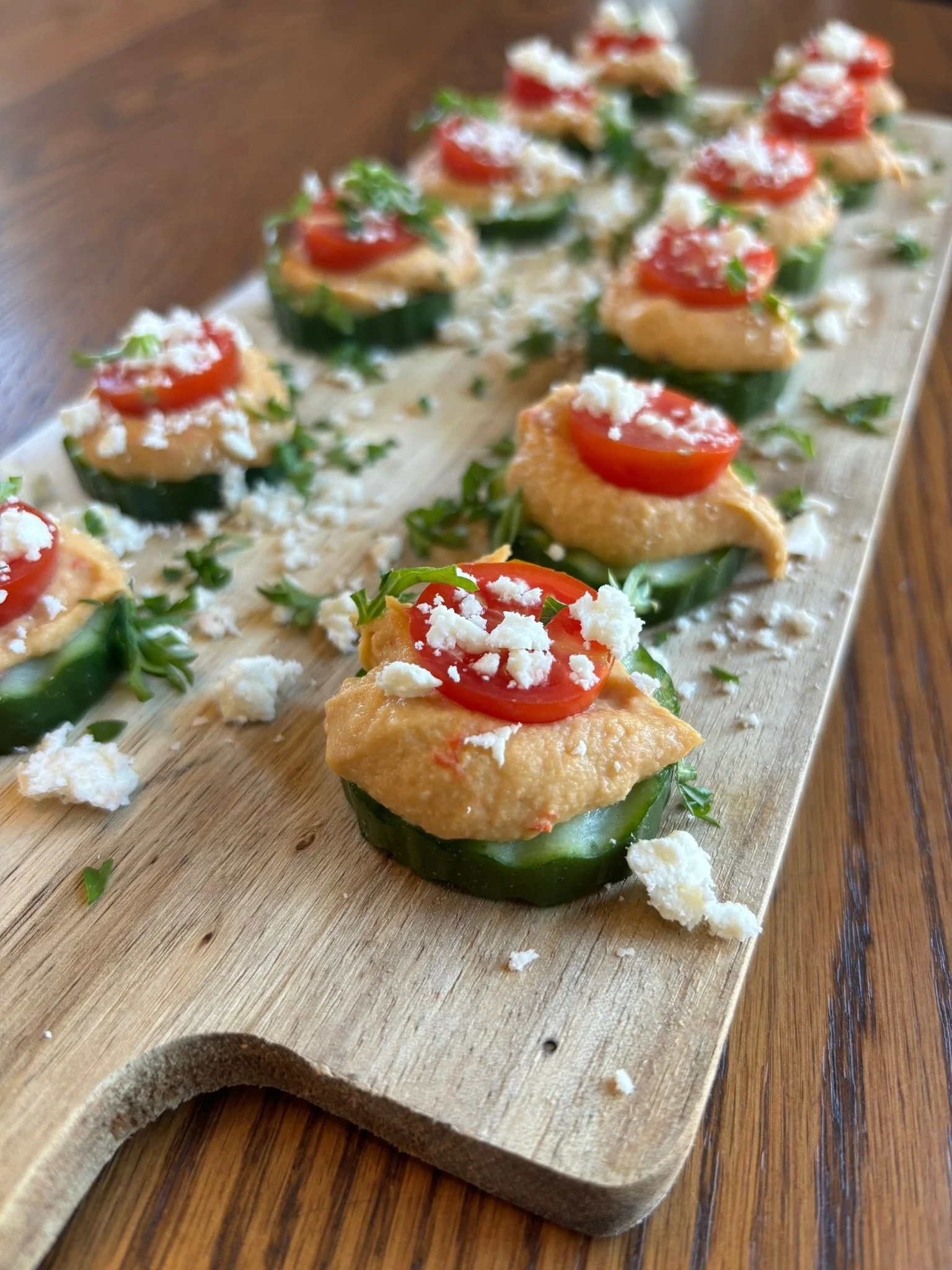 Cucumber slices topped with hummus, cherry tomato, and crumbled feta on wooden board