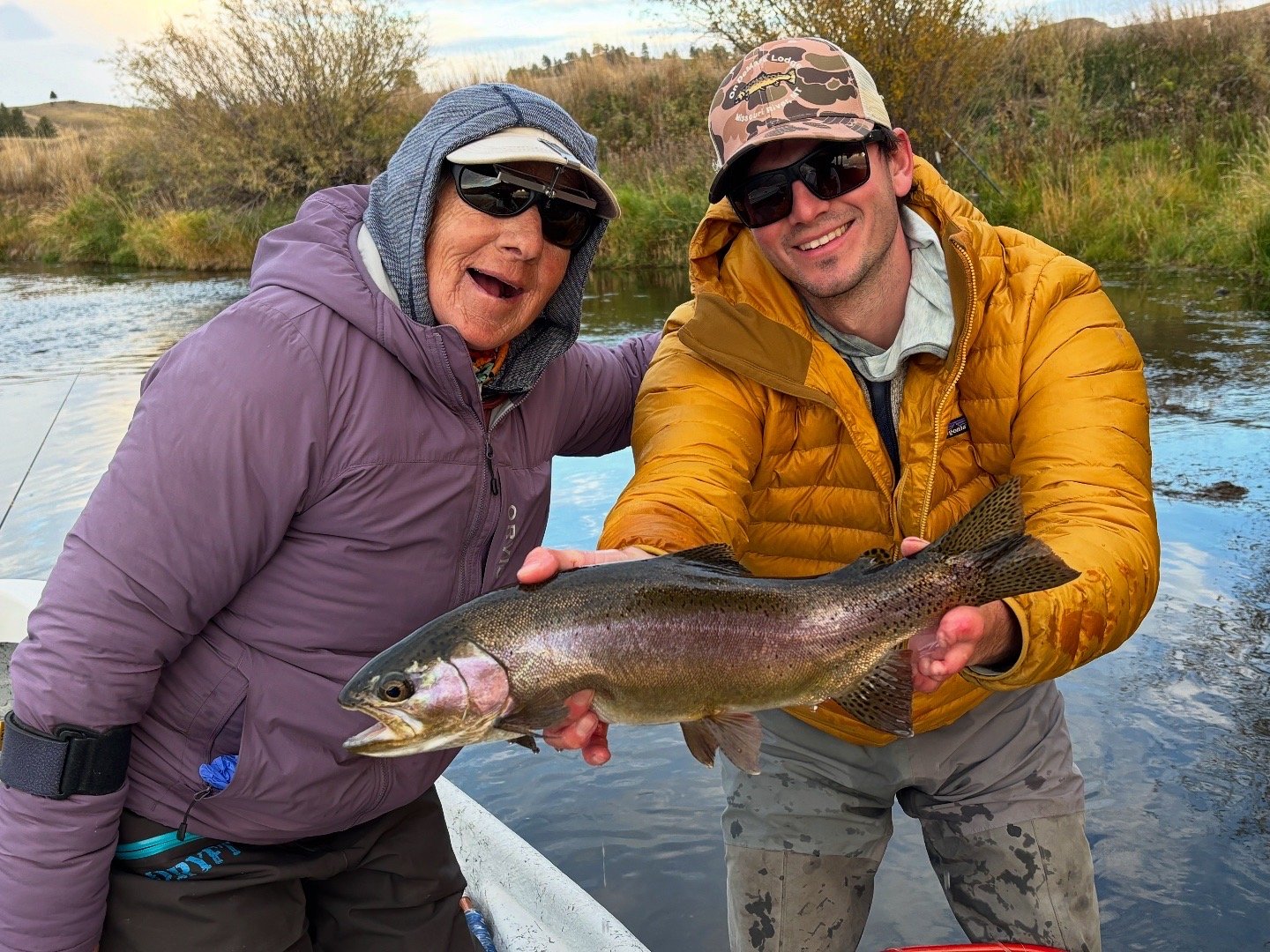 Two anglers holding a rainbow trout on a riverbank