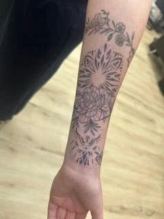 A forearm tattoo featuring floral and geometric patterns.