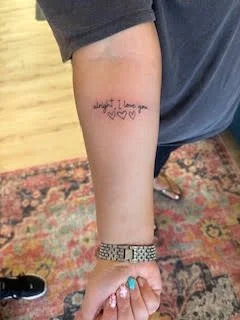 Close-up of a person's forearm with a tattoo that reads 'Angel? I love you' accompanied by two hearts.