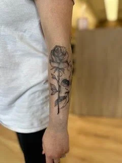 Tattoo of a rose and a butterfly on a person's forearm.