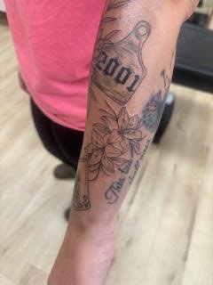 Tattoo of a lily flower, a peace sign, and words on a person's forearm.