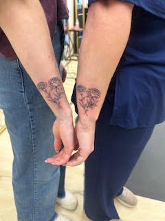 Two people holding hands, each with a tattoo of a tree on their wrist.
