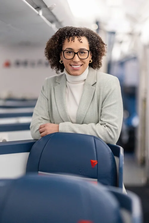 Professional portrait of a smiling woman with glasses in a light blazer inside an aircraft
