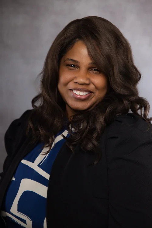Professional portrait of a smiling woman in a black jacket and patterned blue blouse