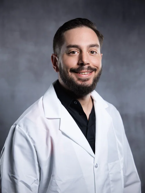 Professional portrait of a smiling man in a white coat against a gray backdrop