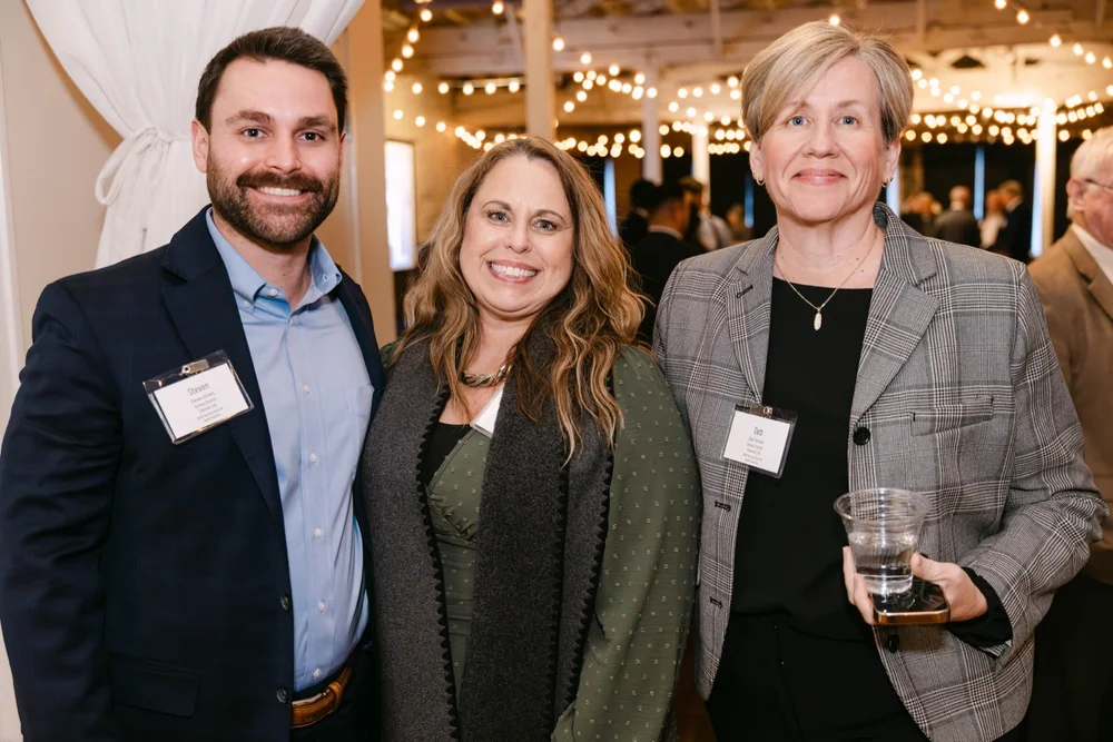 Three smiling attendees wearing name badges at an event