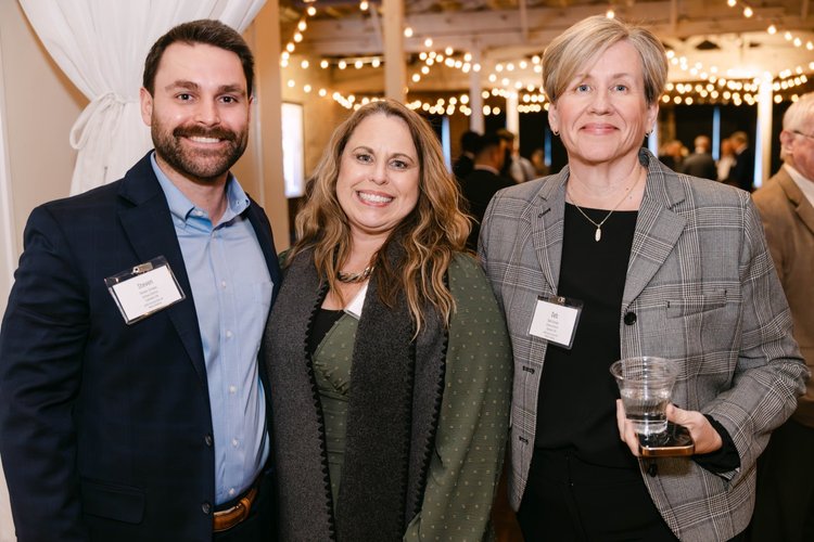 Three smiling attendees wearing name badges at an event