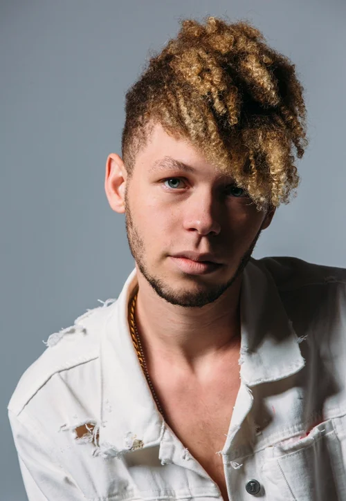 Studio portrait of a man with curly hair in a white jacket against a gray backdrop