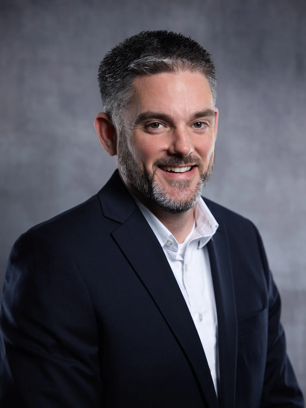 Professional portrait of a smiling man in a dark suit against a gray backdrop