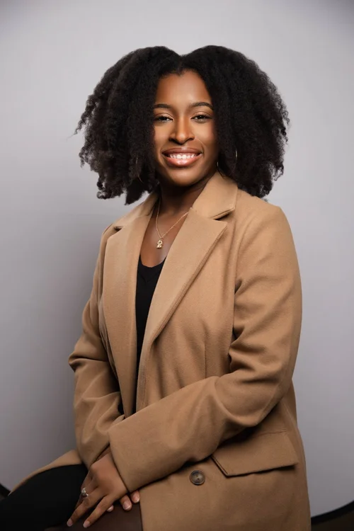 Portrait of a smiling woman in a tan blazer against a light gray backdrop