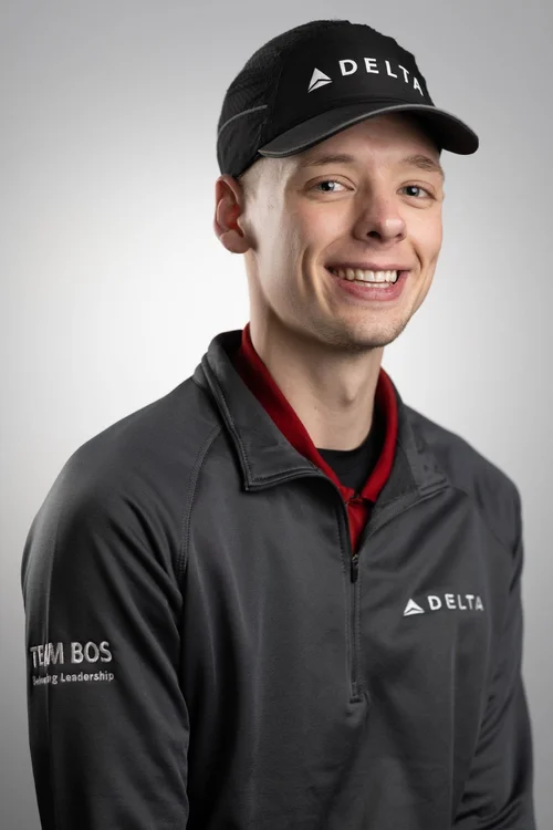 Professional portrait of a smiling man in a black cap and dark jacket against a light gray backdrop