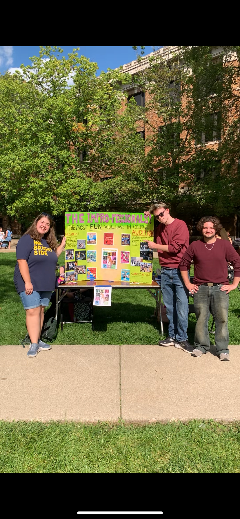 three students outdoors posing in front of a sign for the Impro-fessionals