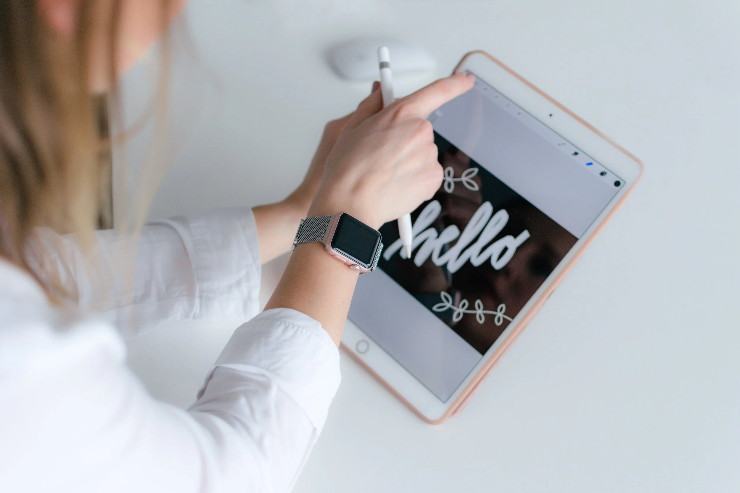 Person using a stylus on a tablet displaying the word 'hello' with decorative leaves.