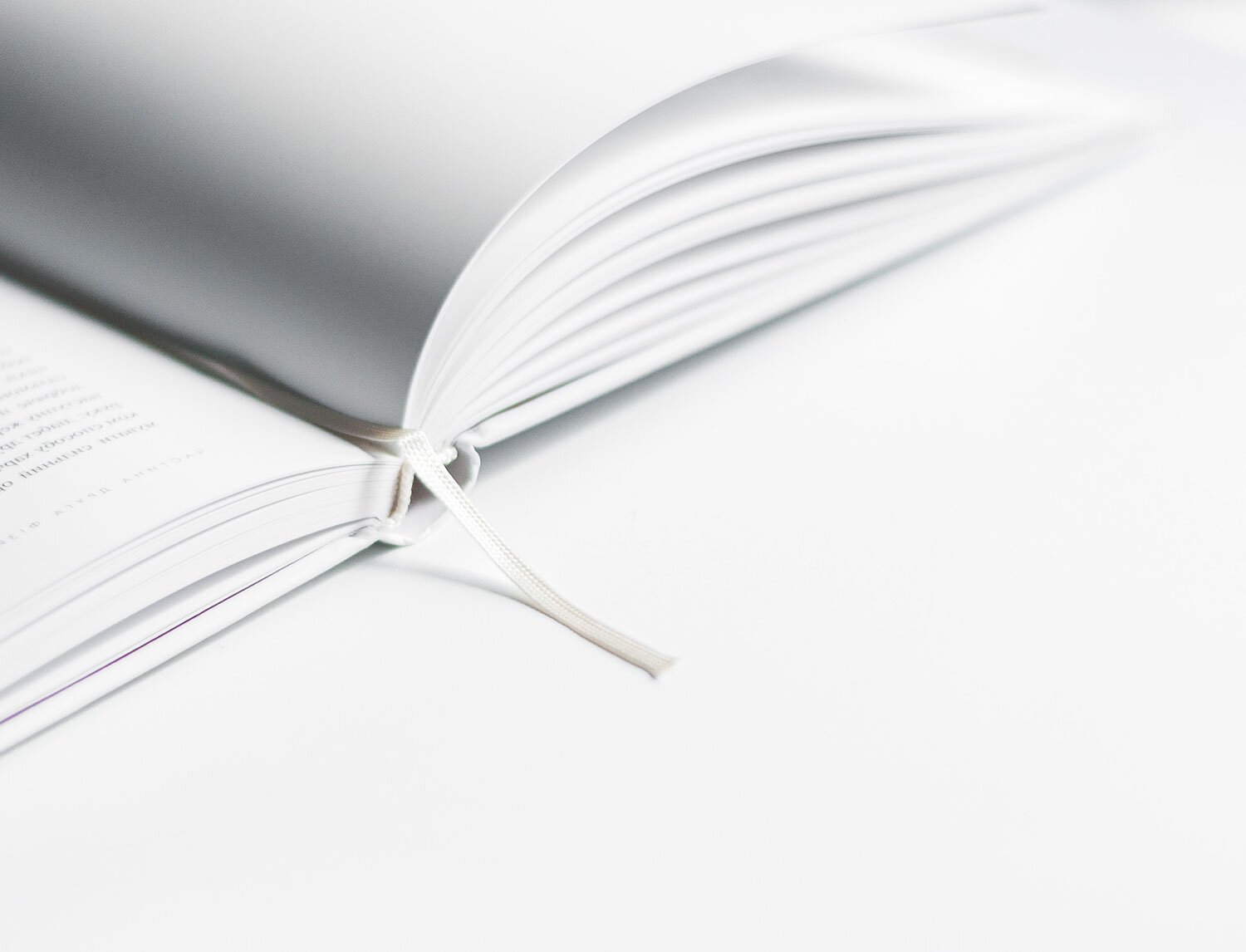 Open, blank notebook with white pages and a white ribbon bookmark on a white background.